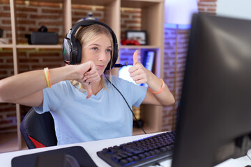 Canvas Print - Young caucasian woman playing video games wearing headphones doing thumbs up and down, disagreement and agreement expression. crazy conflict