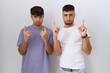 Homosexual gay couple standing over white background pointing up looking sad and upset, indicating direction with fingers, unhappy and depressed.