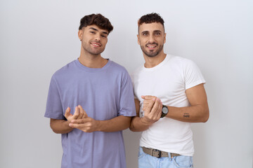 Poster - Homosexual gay couple standing over white background with hands together and crossed fingers smiling relaxed and cheerful. success and optimistic