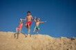 Joyful beach jump of cute kids from sandy dune with clear sky