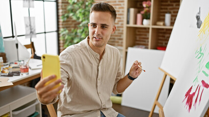 Handsome young man painting in a bright art studio while creating a colorful abstract piece and video blogging.