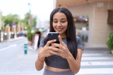 Wall Mural - Young arab woman smiling confident using smartphone at street