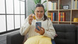 © Krakenimages.com - A mature hispanic woman examines medication while holding a smartphone in a cozy living room setting.