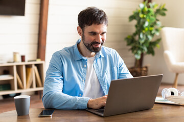 Aufkleber - Businessman is seated at a table, focused on his laptop computer screen, typing on the keyboard as he works or browses online. The table is simple, with no distractions, and the background is plain.