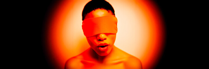 blindfold on young man eyes in spotlight a red / orange studio light