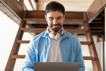 Aufkleber - A man is sitting on stairs, wearing headphones, and focused on using a laptop. He appears engaged in his work or entertainment, typing on the keyboard and looking at the screen intensely