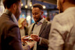 A professional networking scene captures a group of businessmen in smart suits engaged in a conversation over drinks at an upscale indoor venue.