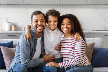 Happy African American family is seated on a comfortable couch. They seem to be engaged in conversation or watching TV together in a cozy living room setting.