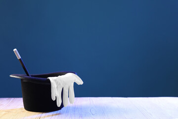 Wall Mural - Magician's hat, wand and gloves on wooden table against blue background, space for text