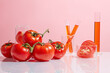 Plenty tomatoes featured on the left side next to some lab glassware with tomato extract over pink background. Copy space for text, front view
