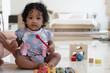 African baby girl  with curly hair holding children's xylophone stick, looking at camera on floor