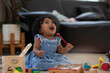 African baby girl with curly hair holding children's xylophone stick, looking at someone with pitiful pleading eyes