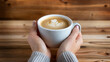 Female hands holding a cup of coffee with latte art on wooden background