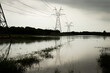 A monochrome image captures a waterlogged expanse, where power lines cast reflections on the flooded field following a heavy spring rain in the Texas Hill Country.