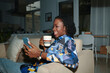 Smiling Black woman reading on couch with cup of coffee and reading news on social media