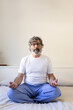 Front view vertical portrait of mature adult man relaxing, doing meditation on bed. Male meditating in the morning.