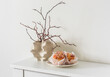 Dry twigs in a creative ceramic vase, fresh brioche buns on a white table. Aesthetic still life