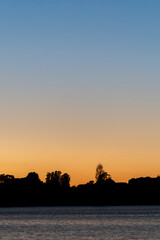 Canvas Print - Silhouette land and trees on horizon under colourful sunrise sky