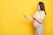 Astonished surprised Caucasian pregnant woman in casual clothing indicating at area for advertising content empty space for promotion posing isolated over yellow background