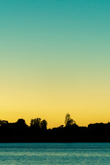 Canvas Print - Silhouette land and trees on horizon under colourful sunrise sky