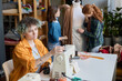 © Mediaphotos - Side view portrait of young woman with prosthetic hand setting up sewing machine in tailoring class workshop copy space
