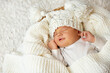 Baby smile in Sleep. Smiling Newborn sleeping on White Blanket in Cradle. Happy Little Child Face in knitted Hat. Cute one month Infant Portrait