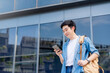 Portrait of handsome Asian student using smartphone. A young man standing outdoor happy smiling with holding mobile phone