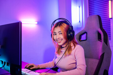 Wall Mural - Happy Gamer endeavor plays online video games tournament with computer neon light, Smiling young woman wearing gaming headphones intend to do playing live stream games online at home looking to camera