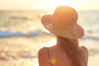 A woman wearing a straw hat is standing on the beach