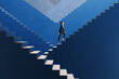 © Who is Danny - Side view happy young businesswoman walking on various blue success stairs on light background. Career ladder and promotion concept.