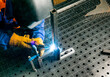 on a metal table, a worker in protective gloves and a helmet welds metal parts