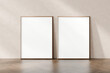 Two empty picture frames leaning against a plain wall on a herringbone parquet floor, awaiting artwork or photographs, 3d render.