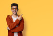 Excited happy curly man wear braces brackets, sunglasses glasses, orange zipup hoodie jaket advertise show point sales slogan text area, isolated yellow background. Dental care, ophthalmology ad.