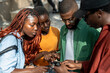 Interested focused four african american students looking online information on smartphone prepare to exam together. Serious attentive group black friends browsing web on mobile phone standing outside