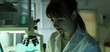 A scientific researcher conducts an experiment in the laboratory. Portrait of a female doctor in a lab coat looking through a microscope