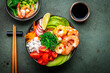 Poke bowl for balanced diet with shrimp, rice, avocado, vegetables and chuka salad, green table background, top view