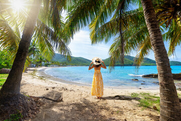 Wall Mural - a woman in a yellow summer dress stands on a tropical paradise beach at the caribbean islands of ant