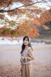 Asian woman in casual dress enjoys a holiday in Japan, walking amid vibrant fall foliage. A cheerful portrait capturing the beauty of nature, fashion, and a journey in Tokyo.