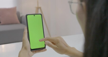 Use green screen for copy space closeup. Chroma key mock-up on smartphone in hand. Woman holds mobile phone and swipes photos or pictures left indoors of cozy home.