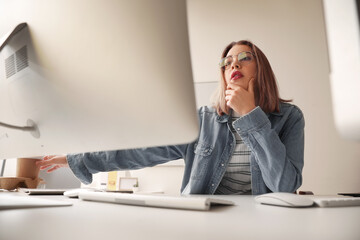 Thoughtful female programmer working with computer at table in office
