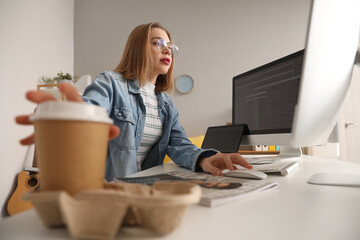 Female programmer taking cup of coffee from table in office