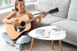 © Pixel-Shot - Young woman playing guitar on her day off at home