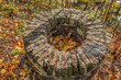 Old brick well in the park on Pelczynski or Poznanska Hill in Lviv, Ukraine. Top view of an old abandoned well with yellow fallen maple leaves inside a round hole in the autumn forest