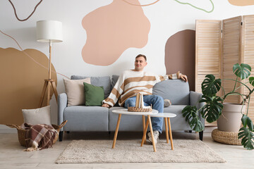 Poster - Young man sitting on sofa in living room