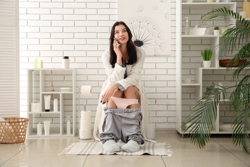 Canvas Print - Young woman talking by mobile phone on toilet bowl in restroom