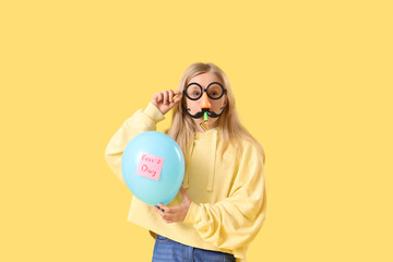 Wall Mural - Little girl in funny disguise with balloon on yellow background. April Fools' Day celebration