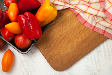 Cutting board with assort of different tomatoes and bell pepper on white wooden background..