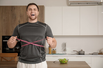 Sporty young man measuring his waist in kitchen. Weight loss concept