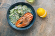 Blue bowl with cucumber salad and grilled salmon on a light-brown granite background, horizontal shot with space, above view