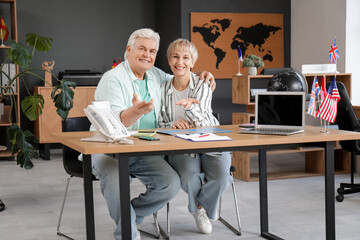 Wall Mural - Happy mature couple hugging at table in travel agency